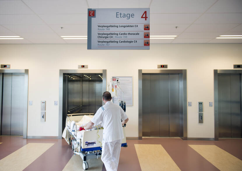 Lifthal in ziekenhuis, patiënt in ziekenhuisbed gaat met verpleger in de lift
